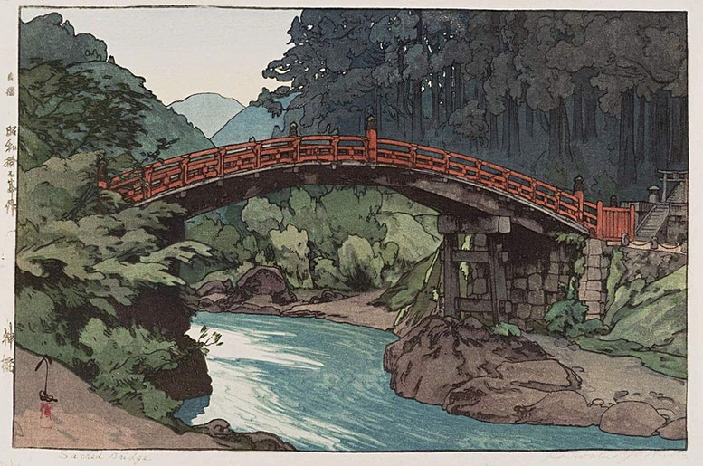 An image of the woodblock print of Sacred bridge by Yoshida Hiroshi showing a wooden arched bridge with red wooden railings crossing over a gently flowing blue stream with green forests on both sides and hills visible in the distance.